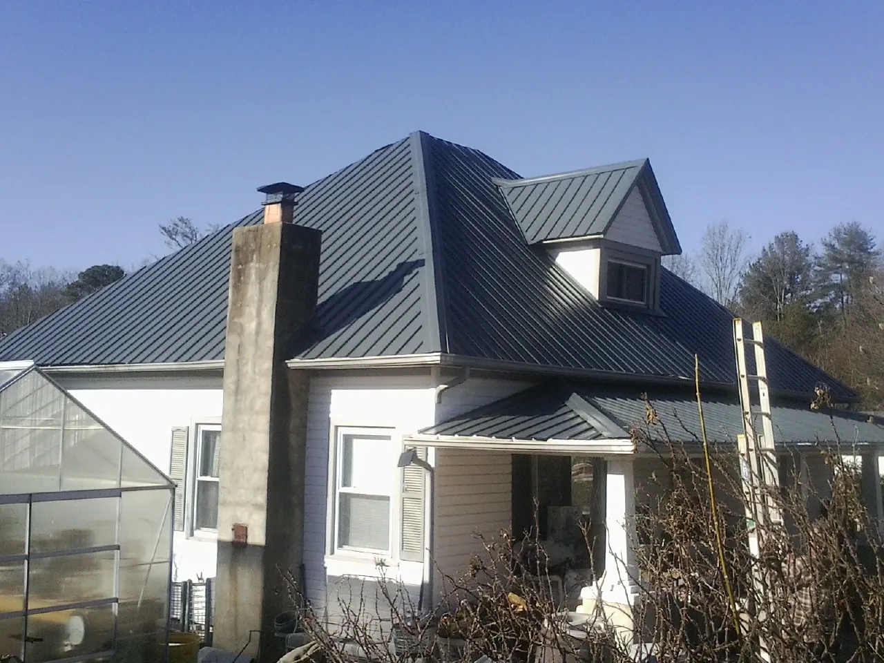 Dark blue standing seam metal roof on a white farmhouse with dormer — Slate & Tile Roof Repair by Roofing Brothers in West Jefferson