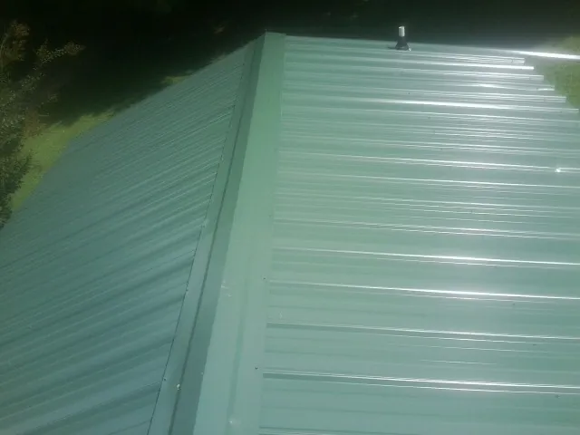 New green metal panels meeting at the ridge of a roof — Flat Roof Repair work by our crew in West Jefferson